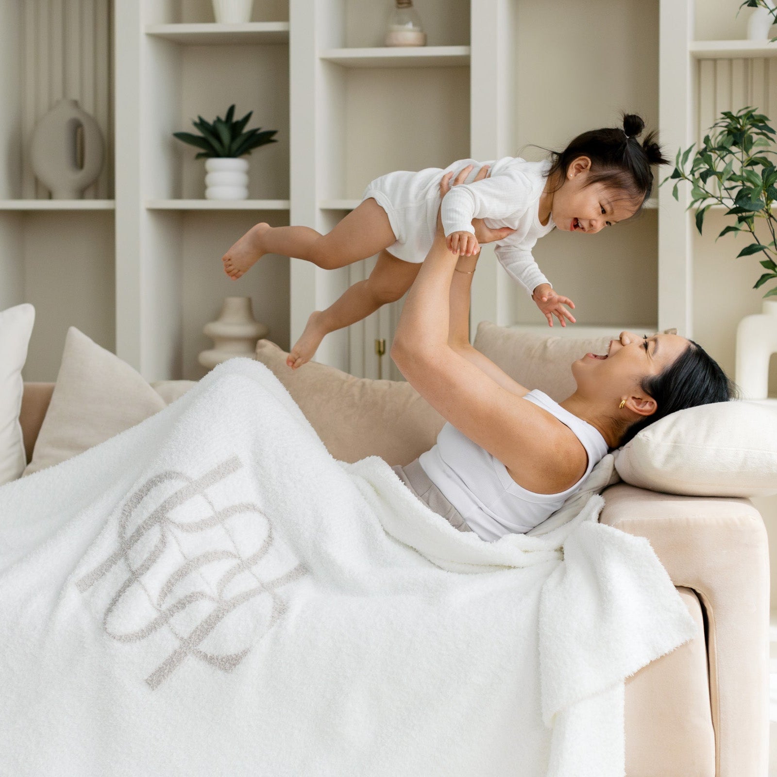 Woman lying on a couch with a child playfully interacting, surrounded by a cozy living room setting.